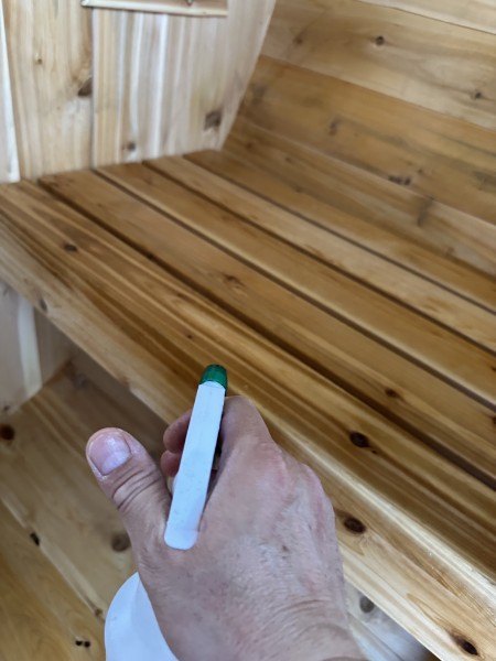 A hand spraying down the cedar sauna bench while cleaning it