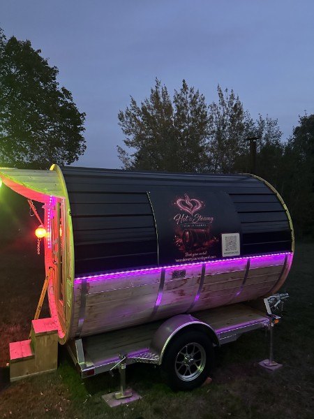 The Hot & Steamy barrel sauna on its trailer at dusk, lit with a purple LED strip