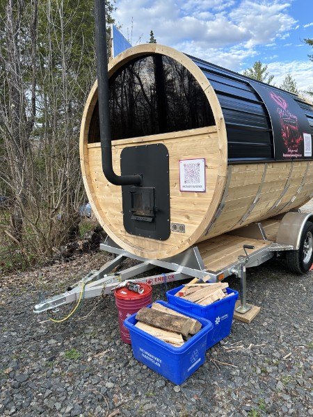 The back of the barrel sauna showing the wood stove chimney, with bins of firewood ready